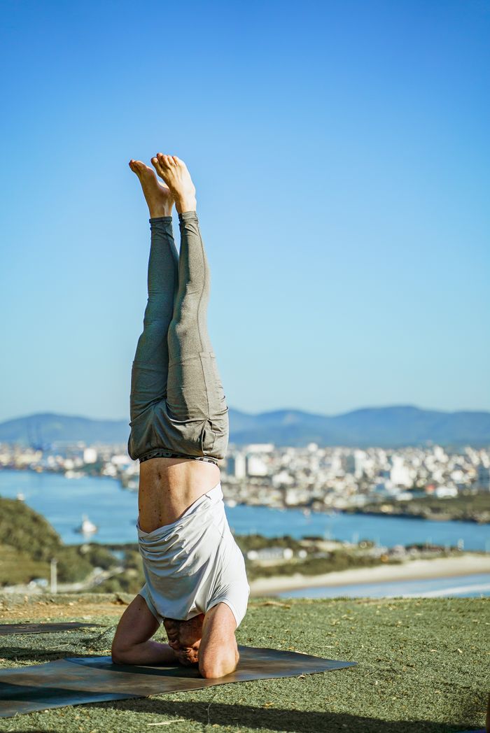 Man performing a headstand yoga pose outdoors on a sunny day with city skyline.