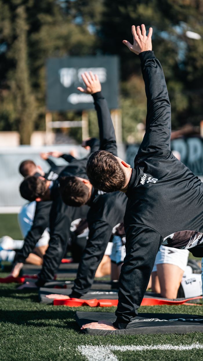 Services A group of athletes perform stretching exercises on a field outdoors. Fitness and teamwork concept.